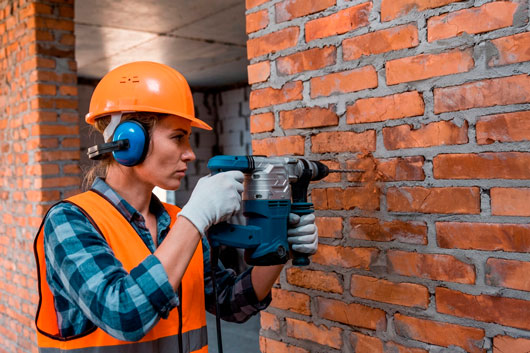Trabajadora de la construcción perforando una pared de ladrillos